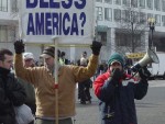 Michael Marcavage holds a banner which reads, "Why Should God Bless America?" as Jason Storms preaches to a crowd gathered at a security checkpoint at President Bush's Inauguration in Washington, D.C.